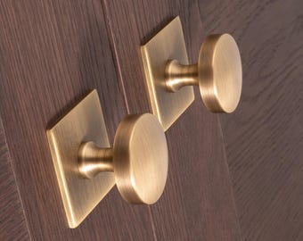 Massief messing kastknop op een vierkante achterplaat. Een ronde knop op een voetstuk. Eenvoudig maar prachtig ontwerp. Modern en eigentijds.