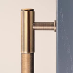 May include: Close-up of a bronze-colored door handle with vertical ribbed detailing on the main body and a cylindrical base. The handle is attached to a blue door frame, set against a neutral background.