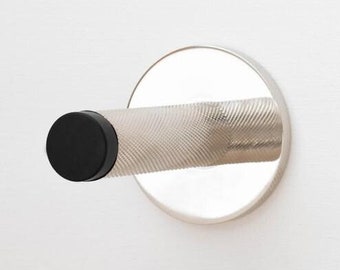 Puede incluir: Un tope de puerta cromado con un mango texturizado y un extremo de goma negro, montado en una puerta blanca. El tope de puerta tiene una base circular y está diseñado para evitar que una puerta se cierre de golpe.
