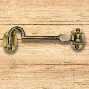 May include: A brass door latch with a curved hook and a lever handle. The latch is mounted on a wooden surface.
