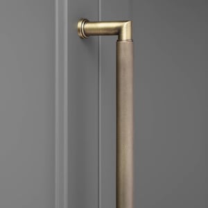 May include: A long, cylindrical cabinet handle with a brushed antique brass finish. The handle features a distinct knurled, cross-hatched texture along its entire length and is attached to a vertical surface by a single right-angled mounting post.