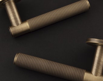 May include: Two cylindrical door handles with a brushed bronze finish. Each handle features a circular mounting plate and a textured, cross-hatched knurled grip section that spans the majority of the handle length, ending in a smooth base.