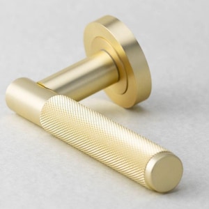 May include: A gold-colored door handle with a textured grip. The handle has a cylindrical shape with a round base and a circular backplate. The metal hardware is designed for interior doors.