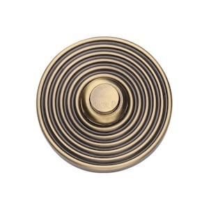 May include: A round, brass doorbell button with concentric circles. The button has a smaller, round, recessed area in the center.
