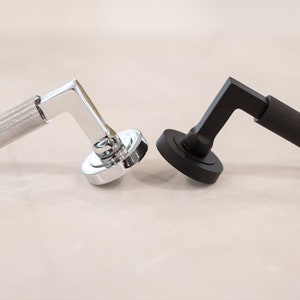 May include: Two door handles, one silver and one black, with a textured grip. Both handles have a round base.