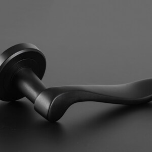 May include: A black door handle with a curved lever. The handle is made of metal and has a smooth finish.