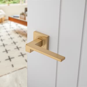 May include: A gold door handle with a square backplate. The handle is made of metal and has a brushed finish.