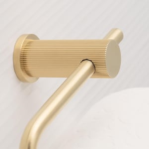 May include: A gold-colored, modern towel rack. The rack features a cylindrical, horizontally-oriented bar with fine, parallel grooves, and a curved arm extending downwards. The rack is mounted on a white wall.