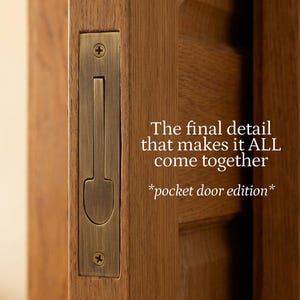Puede incluir: Un tirador rectangular de latón para puerta corredera con asa vertical, fijado con dos tornillos en una puerta de madera. El texto dice: The final detail that makes it ALL come together *pocket door edition*.