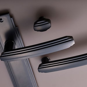 K&ouml;nnte beinhalten: Schwarzes T&uuml;rgriff-Set mit einer rechteckigen Grundplatte und zwei Hebelgriffen. Die Griffe haben einen dekorativen Art-Deco-Stil.