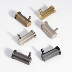 May include: Six metal hooks in different finishes: brass, nickel, black, and silver. Each hook has a cylindrical shape with a ribbed texture and a small hook at the end.