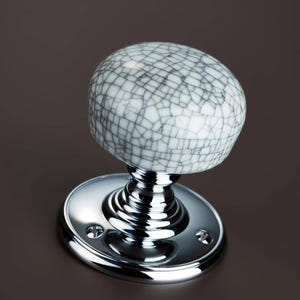 Può includere: Una maniglia per porta in ceramica bianca con una finitura craquelé e una base cromata. La maniglia è rotonda e ha una superficie liscia. La base è circolare e ha una finitura lucida.