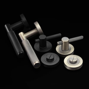 May include: An assortment of door handles in various metallic finishes, including black, silver, and bronze. The handles have textured grips and circular backplates. The background is solid black.