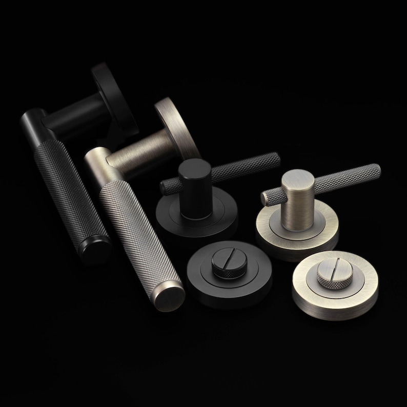 May include: An assortment of door handles in various metallic finishes, including black, silver, and bronze. The handles have textured grips and circular backplates. The background is solid black.