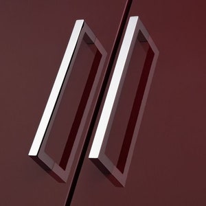 Puede incluir: Dos tiradores de puerta de armario rectangulares plateados con bordes redondeados.