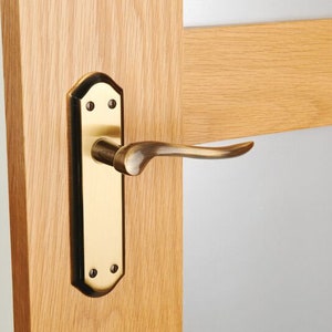 May include: A brass door handle with a curved lever and a rectangular backplate. The handle is mounted on a wooden door.
