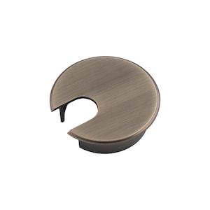 Puede incluir: Un pasacables de escritorio de color bronce con un diseño circular y una abertura curva para la gestión de cables. El pasacables tiene un acabado metálico liso y un borde elevado.