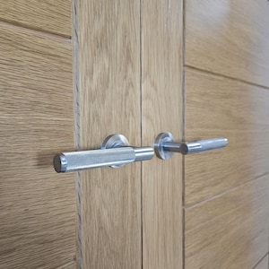 May include: Close-up of a pair of wooden doors with silver metal door handles. The handles have a textured, knurled grip and a cylindrical end. The doors are made of light-colored wood with horizontal grain.