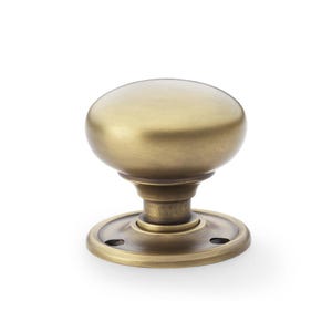 May include: A brass door knob with an oval handle and a circular base. The knob has a classic design with a slightly aged appearance, suggesting a vintage or antique style. The base features small screw holes.