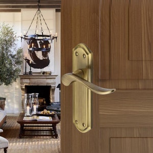 May include: A brass door handle with a curved lever and a square backplate. The handle is mounted on a wooden door.