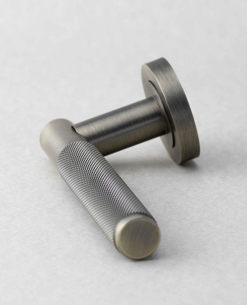 May include: A close-up of a bronze-toned door handle. The handle features a textured grip with a circular end cap. The base of the handle is a circular plate. The hardware is made of metal and has a vintage aesthetic.