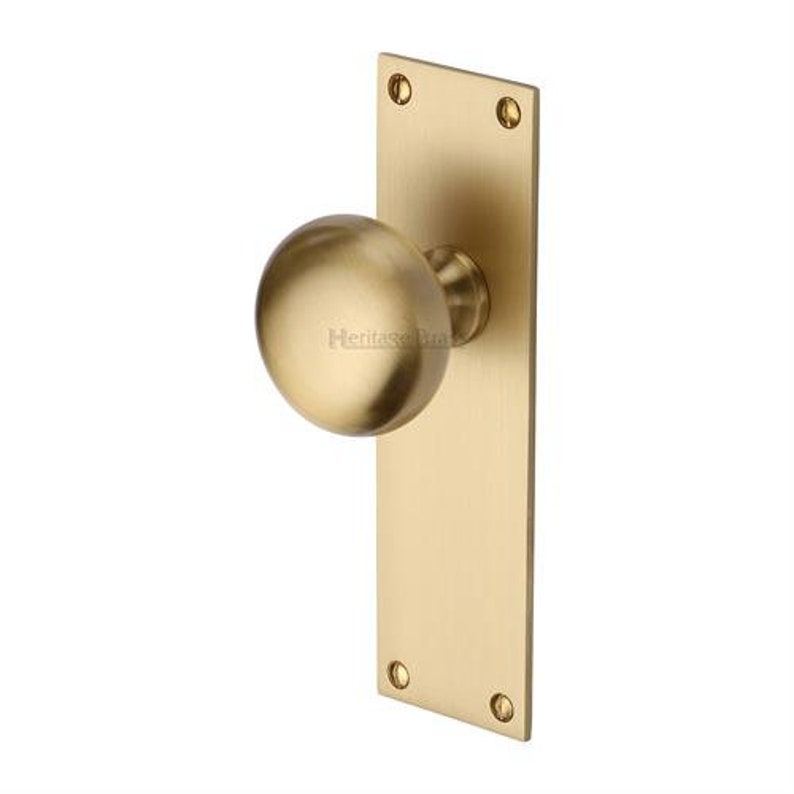 Peut inclure: Un bouton de porte en laiton avec une poign&eacute;e ronde et une plaque arri&egrave;re rectangulaire. La quincaillerie de porte a une finition bross&eacute;e et est fix&eacute;e avec quatre vis. La marque "Heritage Brass" est visible sur le bouton.