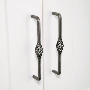 May include: Two black metal cabinet pulls with a twisted wire design. The pulls are mounted on a white cabinet door.