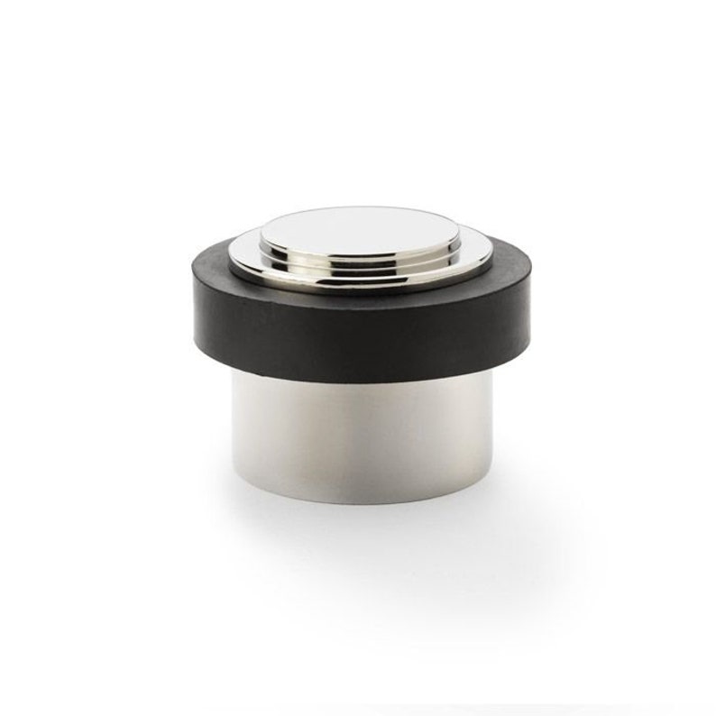May include: A chrome doorstop with a black rubber base. The doorstop has a rounded top and a cylindrical base.