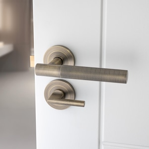 May include: A brushed nickel door handle with a square lever and a round knob. The handle is mounted on a white door.