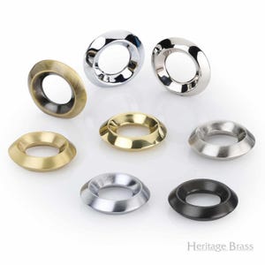 May include: Collection of decorative metal eyelets in various finishes, including polished chrome, antique brass, and matte black. The eyelets have a circular design with a flared outer edge, suitable for various craft and design projects.