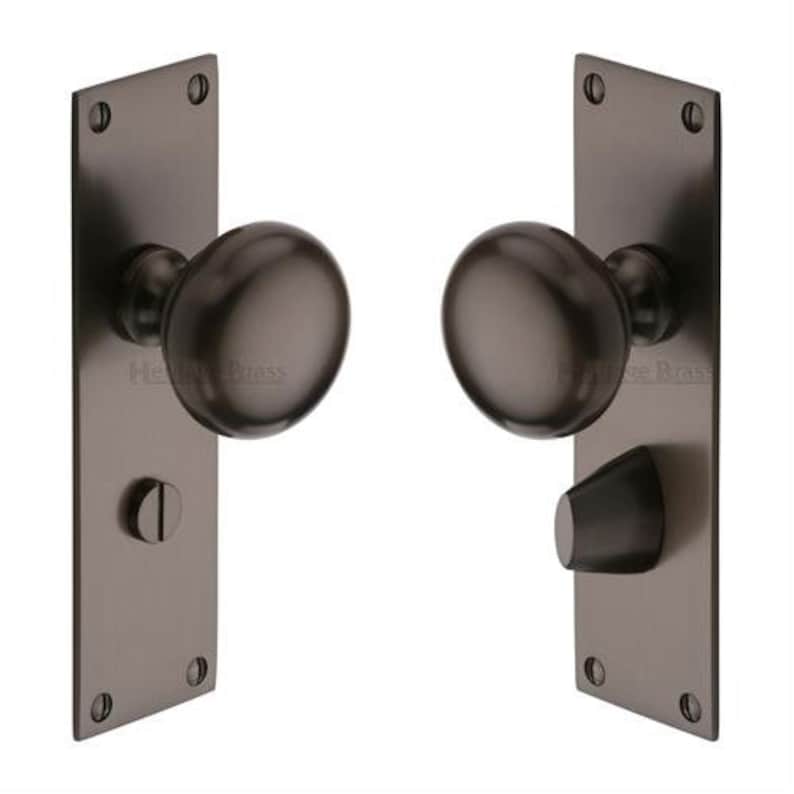 Peut inclure: Deux poign&eacute;es de porte en bronze fonc&eacute; avec plaques rectangulaires. Chaque bouton est de forme ovale. Les plaques ont des coins arrondis et sont fix&eacute;es avec quatre vis. Une plaque a un petit levier inclin&eacute;.