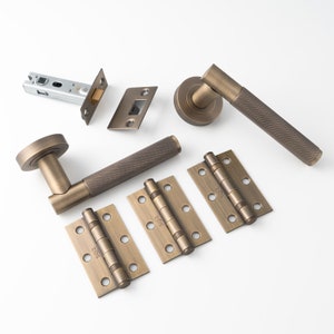 May include: A set of antique brass door hardware, including two door handles, a door latch, a door strike plate, and three pairs of hinges. The handles have a textured, knurled design.