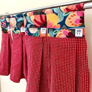 K&ouml;nnte beinhalten: Vier rote K&uuml;chent&uuml;cher mit wei&szlig;en Punkten und floral gemusterten Stoffoberteilen. Die Handt&uuml;cher h&auml;ngen an einer silbernen Stange. Die Stoffoberteile haben den Text "DD" und "WOOD POINT" aufgedruckt.