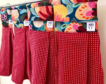 Puede incluir: Cuatro toallas de cocina rojas con lunares blancos y tapas de tela con estampado floral. Las toallas están colgadas de una barra plateada. Las tapas de tela tienen el texto "DD" y "WOOD POINT" impreso en ellas.