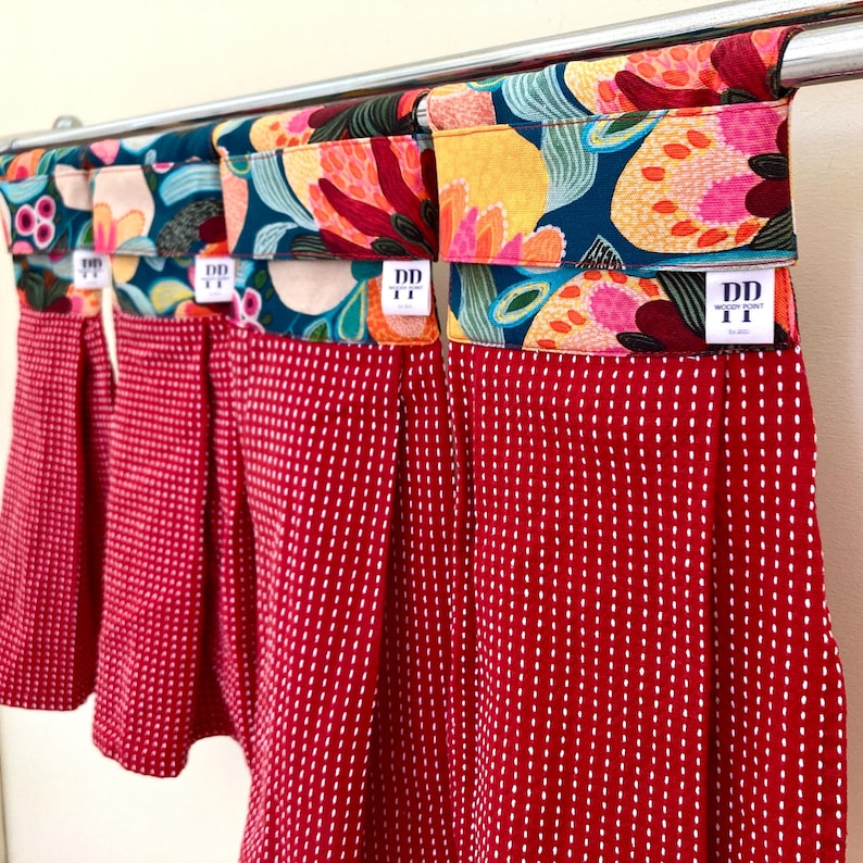 K&ouml;nnte beinhalten: Vier rote K&uuml;chent&uuml;cher mit wei&szlig;en Punkten und floral gemusterten Stoffoberteilen. Die Handt&uuml;cher h&auml;ngen an einer silbernen Stange. Die Stoffoberteile haben den Text "DD" und "WOOD POINT" aufgedruckt.