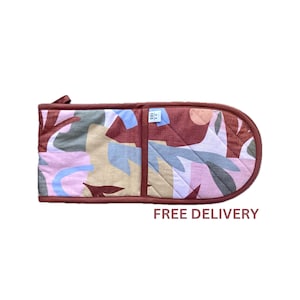 May include: A double oven glove with a vibrant abstract design in brown, pink, blue, and beige. It features a hanging loop and a dark brown trim. The text "FREE DELIVERY" is printed at the bottom. The oven glove is designed for kitchen use.