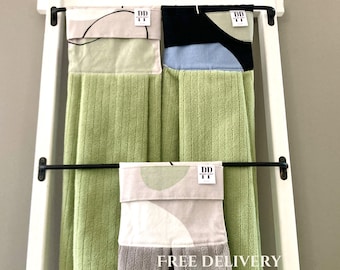 Puede incluir: Tres toallas de cocina colgadas en una escalera blanca. Las toallas son verdes, grises y blancas con patrones abstractos. Las toallas tienen una etiqueta en blanco y negro que dice "DD Design". La toalla de abajo tiene el texto "ENVÍO GRATIS" impreso en ella.