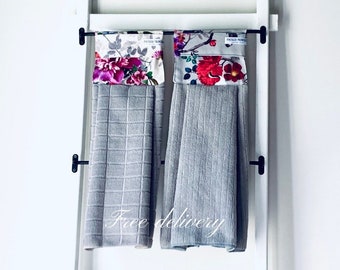 Puede incluir: Dos toallas de cocina grises con detalles de tela con estampado floral colgadas de un estante blanco. El texto "Entrega gratuita" es visible en la parte inferior central de la imagen.