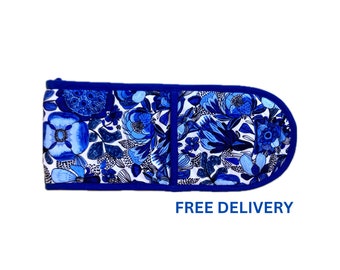Puede incluir: Una manopla doble para horno con fondo blanco y un patrón denso de flores y follaje azul. La manopla tiene un borde de tela azul sólido y un extremo redondeado. El texto FREE DELIVERY está impreso en azul debajo de la manopla.