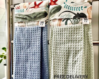 Puede incluir: Dos paños de cocina colgantes con tejido de textura de gofre en azul claro y verde salvia. Las secciones superiores presentan una banda de tela blanca estampada con estrellas de mar rojas, ballenas verdes y algas verde azulado. Etiqueta DD.