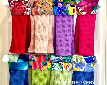 Puede incluir: Ocho paños de cocina de tejido tipo gofre colgados con partes superiores de tela estampada. Los paños son rojos, rosa claro, morados, magenta, azules, verde lima, verde claro y azul oscuro, con estampados florales y tropicales.