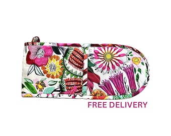 Puede incluir: Una manopla de cocina acolchada con un vibrante estampado floral de ilustraciones botánicas en rosa, naranja, amarillo y verde sobre fondo blanco. La manopla tiene un extremo redondeado y una pequeña trabilla de tela para colgarla.