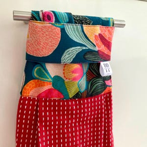 K&ouml;nnte beinhalten: Ein rotes K&uuml;chentuch aus Stoff mit wei&szlig;en N&auml;hten und einem bunten Blumendruck. Das Tuch h&auml;ngt an einem silbernen Handtuchhalter. Das Etikett lautet "DD Wood Tone 11"