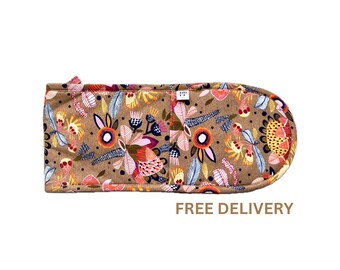 Puede incluir: Un guante de horno marrón con un estampado floral colorido. El guante está hecho de tela y tiene un lazo para colgar.