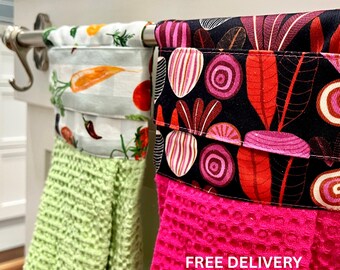 Puede incluir: Dos paños de cocina colgantes con partes superiores de tela con estampados de verduras. Un paño tiene una parte inferior de textura de gofre verde claro con estampado de zanahorias y chiles. El otro tiene una parte inferior rosa brillante con estampado de remolachas.