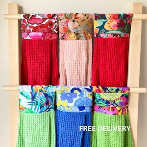 May include: Six kitchen towels hanging on a wooden rack. The towels are made of waffle weave fabric and have different colourful floral patterns on the top. The text "FREE DELIVERY" is visible at the bottom of the image.