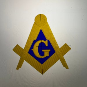 Puede incluir: Símbolo masónico dorado y azul, con compás y escuadra con la letra "G" en el centro. El símbolo está sobre un fondo blanco. El diseño tiene una apariencia texturizada y bordada.