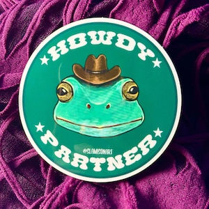 May include: A green frog wearing a brown cowboy hat with the text "HOWDY PARTNER" in white letters on a green circle with white stars.