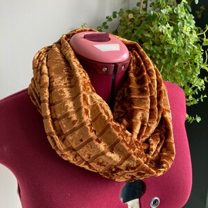 May include: A brown velvet infinity scarf with a textured pattern. The scarf is folded and draped around a mannequin's neck.