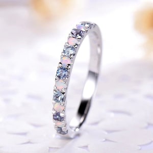 Puede incluir: Un anillo de banda de plata con una fila de piedras de ópalo blanco y topacio azul.